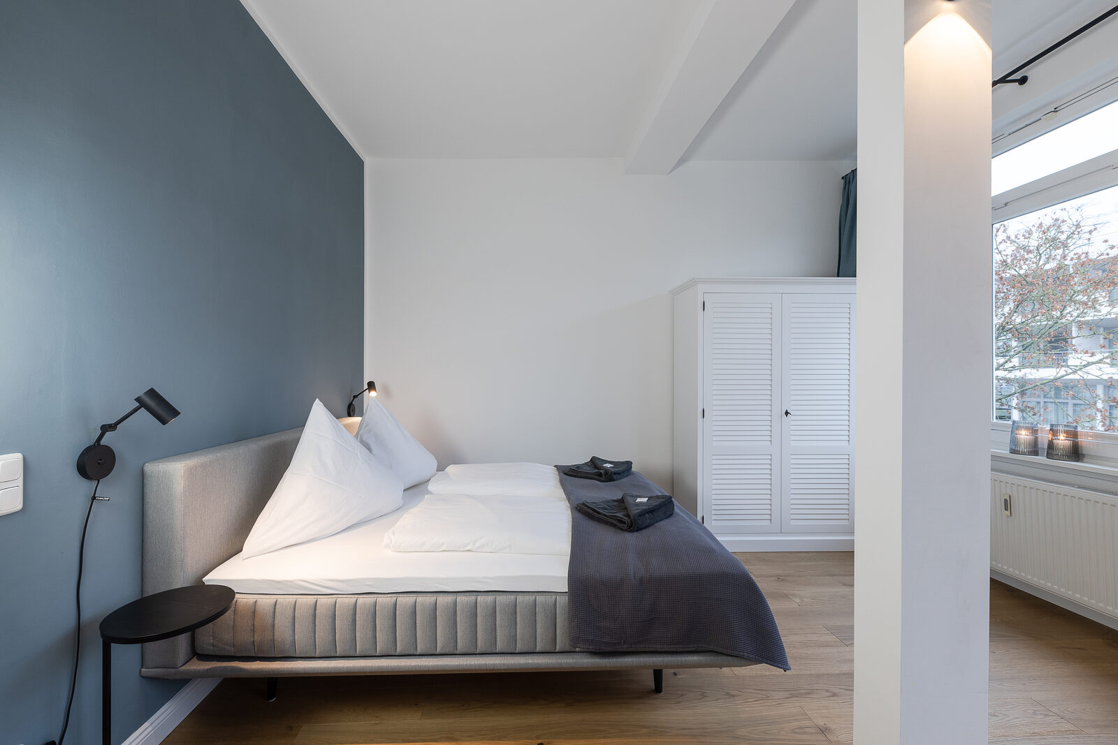 Bett mit Lamellenschrank und Blick zum Fenster